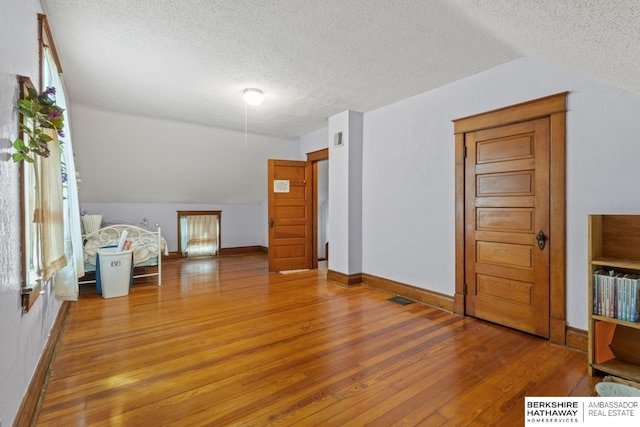 6301 SW 34th Ct, Lincoln, NE 68523 - additional living space with a textured ceiling, visible vents, vaulted ceiling, wood finished floors, and baseboards