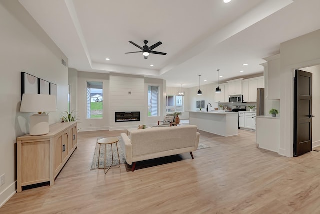 living room with ceiling fan, a fireplace, light wood-type flooring, a tray ceiling, and recessed lighting