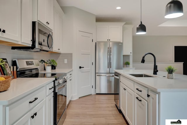 kitchen featuring pendant lighting, a sink, light wood-style flooring, backsplash, and stainless steel appliances