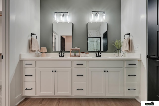 bathroom featuring a sink, baseboards, double vanity, and wood finished floors