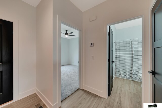 corridor featuring baseboards, light wood finished floors, and visible vents