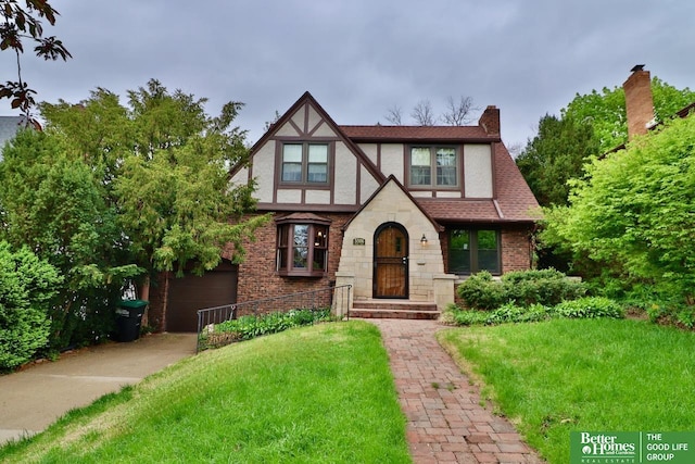 english style home with stucco siding, stone siding, concrete driveway, a chimney, and a front lawn
