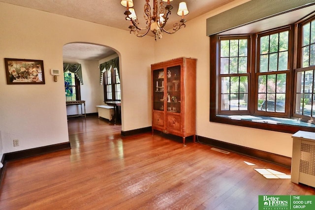 5506 Howard St, Omaha, NE 68106 - unfurnished dining area featuring arched walkways, wood finished floors, radiator heating unit, and baseboards