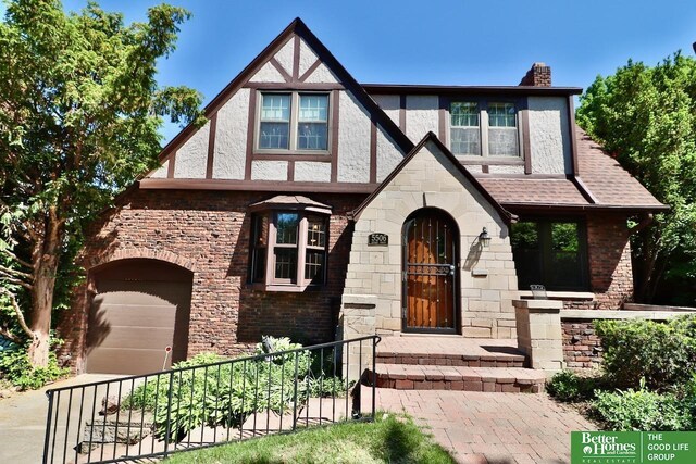 5506 Howard St, Omaha, NE 68106 - tudor home with a chimney, stone siding, a shingled roof, and driveway