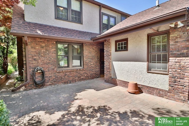 5506 Howard St, Omaha, NE 68106 - view of exterior entry featuring stucco siding, a patio area, brick siding, and roof with shingles