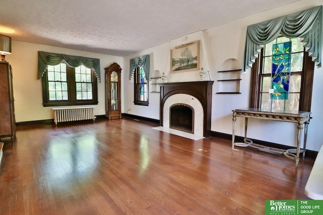5506 Howard St, Omaha, NE 68106 - unfurnished living room with radiator heating unit, wood finished floors, a fireplace with flush hearth, baseboards, and a textured ceiling