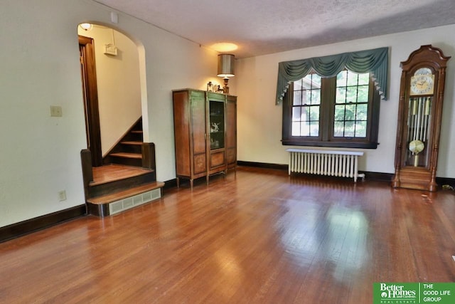 5506 Howard St, Omaha, NE 68106 - unfurnished living room with radiator heating unit, wood finished floors, arched walkways, stairs, and baseboards