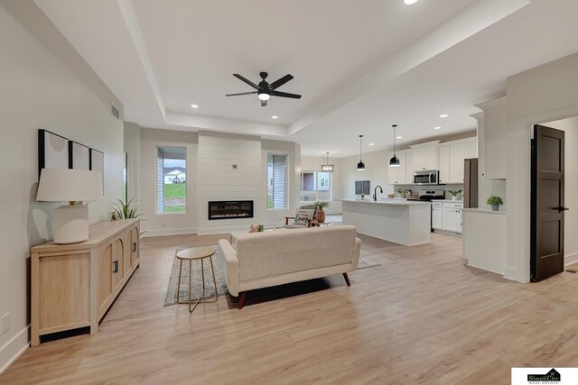 living room with ceiling fan, light wood finished floors, a raised ceiling, a large fireplace, and recessed lighting