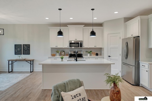 kitchen with appliances with stainless steel finishes, a sink, light countertops, a kitchen island with sink, and tasteful backsplash