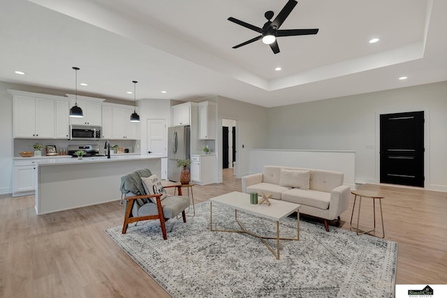 living room featuring ceiling fan, light wood finished floors, recessed lighting, baseboards, and a tray ceiling