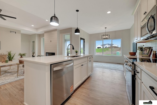 kitchen with appliances with stainless steel finishes, a fireplace, a sink, light wood finished floors, and recessed lighting