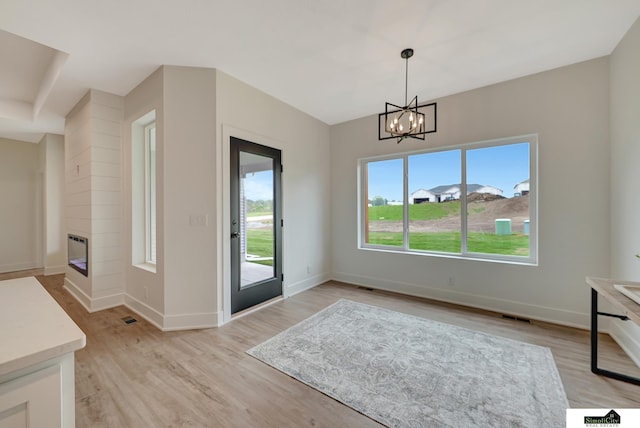 interior space with visible vents, a glass covered fireplace, baseboards, a chandelier, and light wood-style flooring