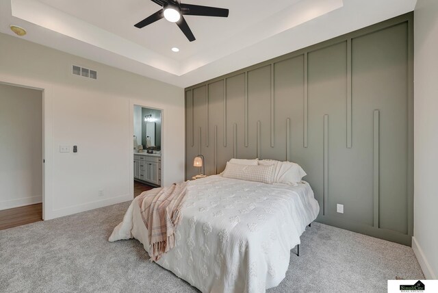 carpeted bedroom with visible vents, a raised ceiling, ensuite bath, and baseboards
