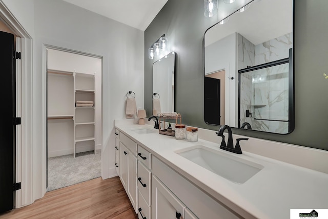 bathroom featuring double vanity, a sink, a marble finish shower, and wood finished floors