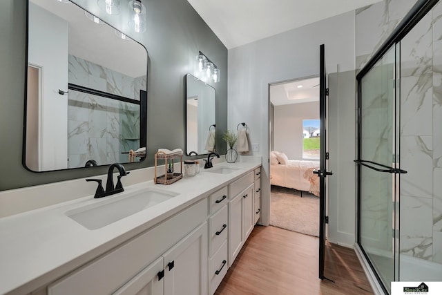 ensuite bathroom with a sink, a marble finish shower, double vanity, and wood finished floors
