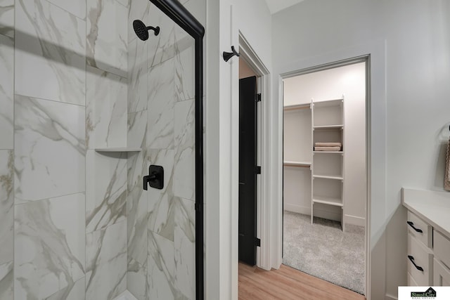 bathroom featuring a marble finish shower, vanity, wood finished floors, and a spacious closet