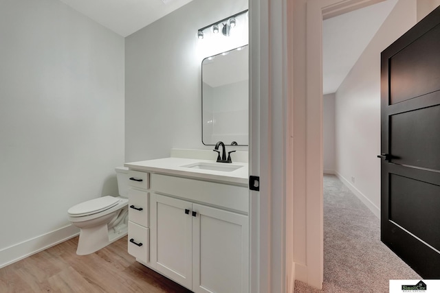 half bathroom with vanity, baseboards, wood finished floors, and toilet
