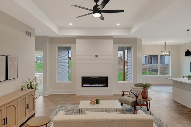 living room featuring a ceiling fan, a tray ceiling, a wealth of natural light, and light wood-style floors