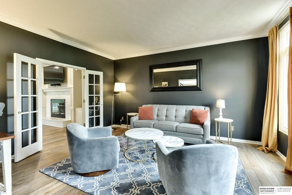 living room with baseboards, a glass covered fireplace, ornamental molding, and wood finished floors