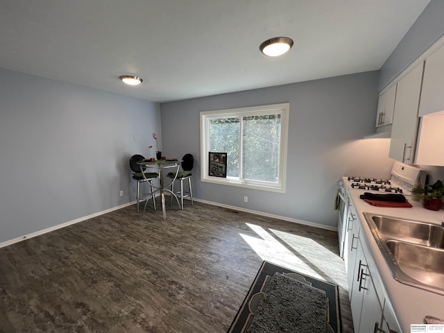 kitchen featuring white gas range oven, baseboards, dark wood-style floors, white cabinetry, and a sink