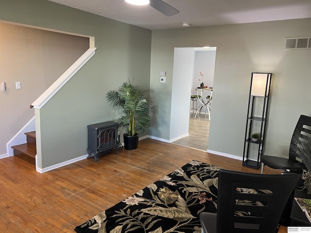 interior space featuring ceiling fan, a wood stove, baseboards, wood finished floors, and stairway