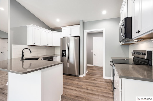 kitchen with a peninsula, light wood-type flooring, white cabinets, a sink, and appliances with stainless steel finishes