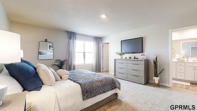 bedroom with baseboards, light carpet, and ensuite bath