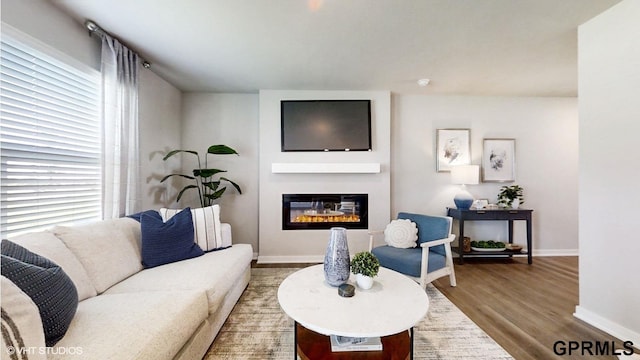 living room with baseboards, a glass covered fireplace, plenty of natural light, and wood finished floors