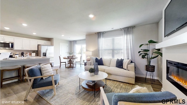 living room featuring baseboards, recessed lighting, light wood-style flooring, and a glass covered fireplace