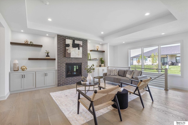 living area with a raised ceiling, light wood finished floors, recessed lighting, baseboards, and a brick fireplace