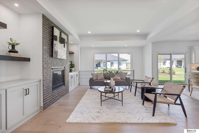 living room with a fireplace, light wood-style floors, a raised ceiling, and recessed lighting