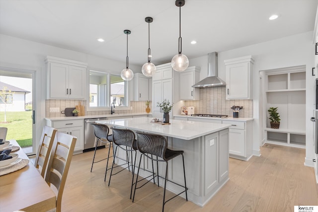 kitchen with wall chimney exhaust hood, appliances with stainless steel finishes, a kitchen island, a breakfast bar, and light wood-type flooring