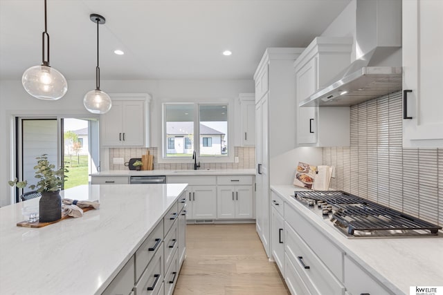 kitchen featuring wall chimney exhaust hood, appliances with stainless steel finishes, a sink, recessed lighting, and white cabinetry