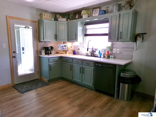 kitchen with light wood-style floors, backsplash, light countertops, a sink, and dishwashing machine