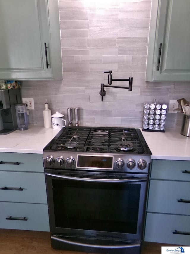 kitchen featuring stainless steel range with gas stovetop, gray cabinets, light stone countertops, and tasteful backsplash