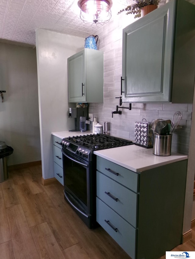 kitchen featuring stainless steel range with gas cooktop, backsplash, wood finished floors, and gray cabinetry