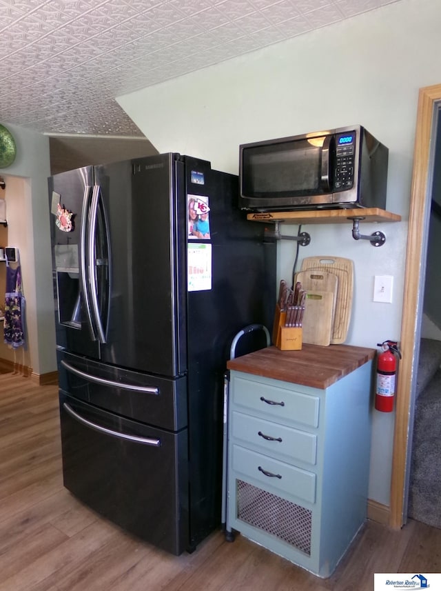kitchen with stainless steel microwave, light wood-type flooring, baseboards, and black fridge with ice dispenser