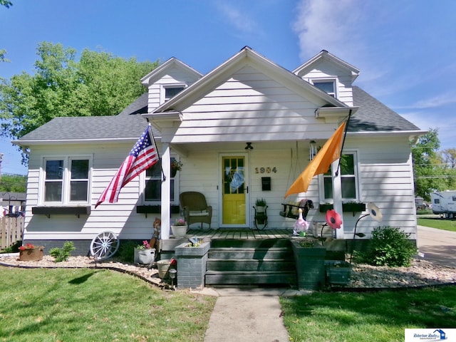 view of front facade with a porch, roof with shingles, and a front yard