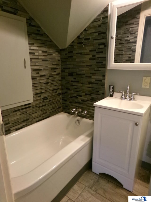 full bath with a bathing tub, lofted ceiling, and vanity