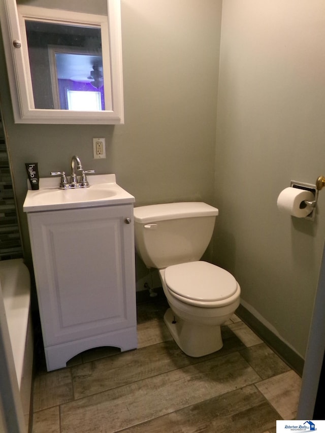 bathroom featuring vanity, baseboards, wood finished floors, and toilet