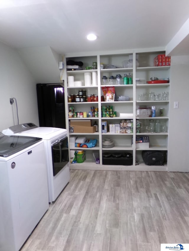 clothes washing area with laundry area, washing machine and dryer, and light wood-style flooring