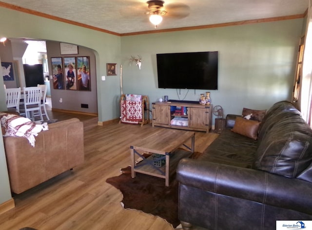 living area with ornamental molding, wood finished floors, baseboards, arched walkways, and a ceiling fan