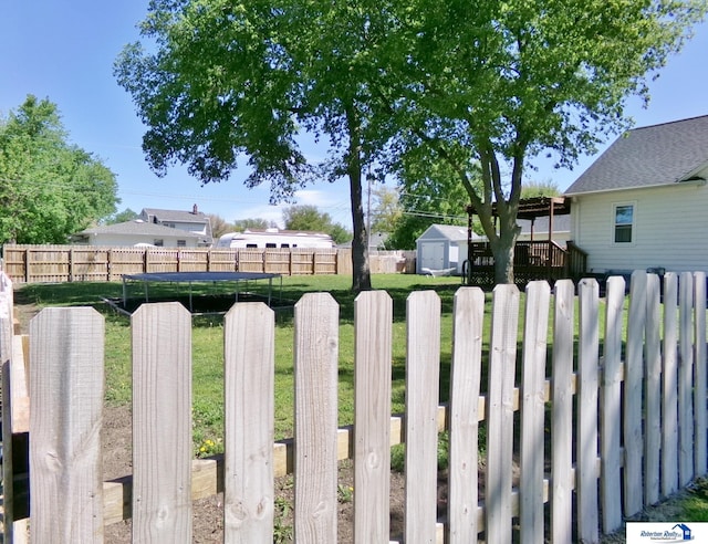 view of yard with a fenced backyard, a storage unit, a trampoline, and an outbuilding