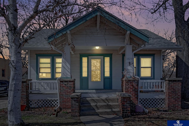 doorway to property featuring roof with shingles and covered porch