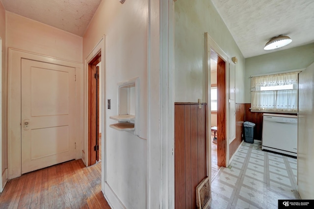 corridor with visible vents, a textured ceiling, wainscoting, and light wood-style floors