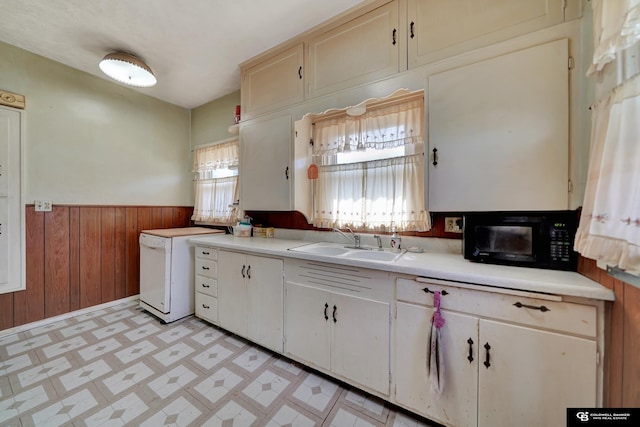 kitchen with black microwave, wainscoting, a sink, light countertops, and light floors