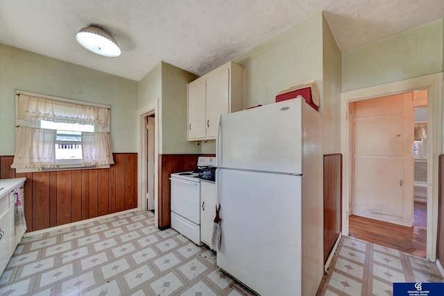 kitchen featuring wood walls, white appliances, light floors, white cabinetry, and a wainscoted wall
