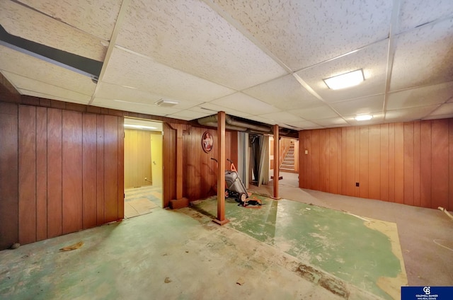 finished basement with wooden walls, a drop ceiling, and stairs