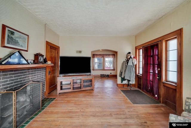 entryway with a brick fireplace, a textured ceiling, visible vents, and wood finished floors
