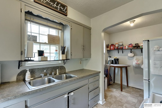 kitchen with a sink, baseboards, freestanding refrigerator, and arched walkways